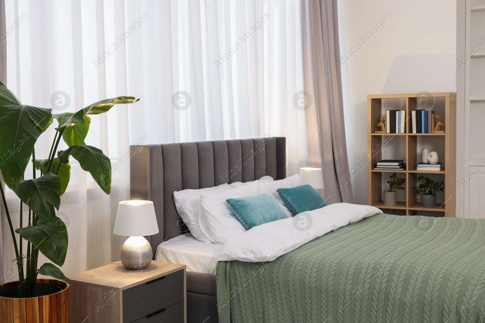 Photo of Comfortable bed with bedding, houseplants and books in room