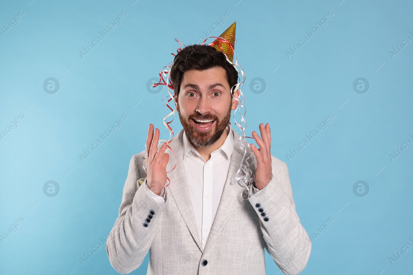 Photo of Emotional man with serpentine streamers on light blue background
