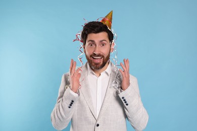 Emotional man with serpentine streamers on light blue background