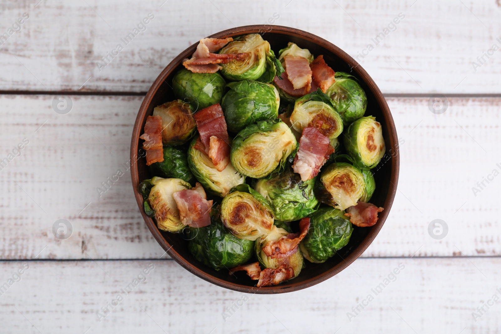 Photo of Delicious roasted Brussels sprouts and bacon in bowl on light wooden table, top view