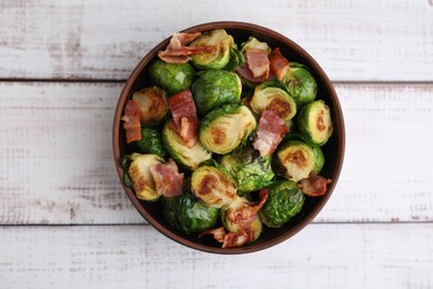 Delicious roasted Brussels sprouts and bacon in bowl on light wooden table, top view