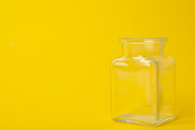 Photo of Open empty glass jar on yellow background, space for text