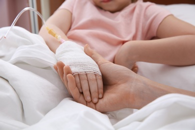 Doctor holding little child's hand with intravenous drip in hospital, closeup