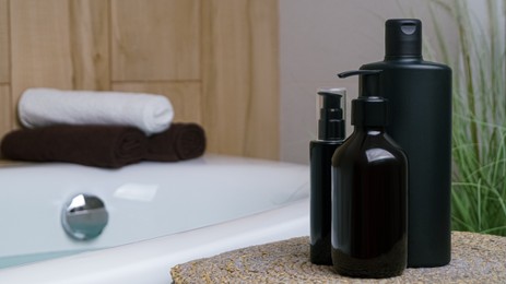 Photo of Bottle of bubble bath and cosmetic products on wicker mat near tub indoors, space for text