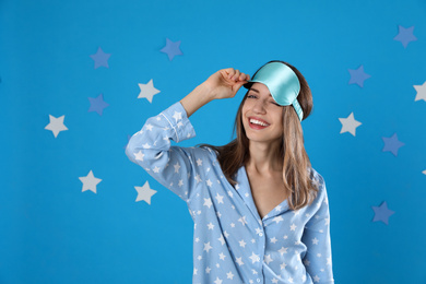 Photo of Beautiful woman wearing pajamas and sleep mask on light blue background. Bedtime