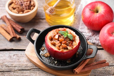 Photo of Tasty baked apple with nuts in baking dish, honey and cinnamon sticks on wooden table, closeup