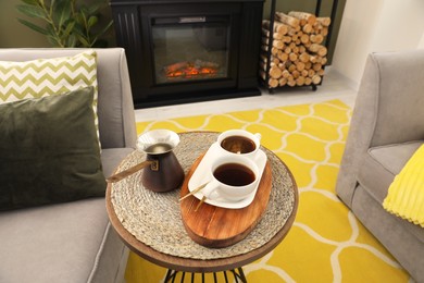 Cups of coffee and cezve on table near fireplace in living room