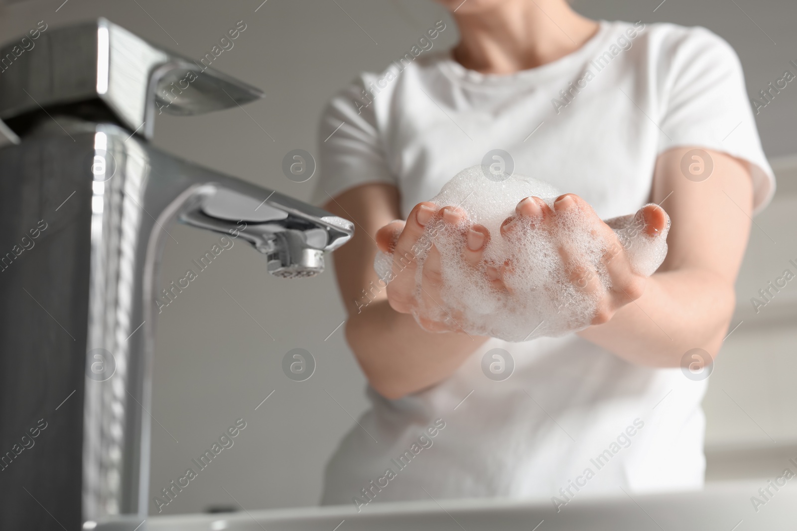 Photo of Woman washing hands with cleansing foam near sink in bathroom, closeup