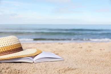 Photo of Open book and hat on sandy beach near sea. Space for text