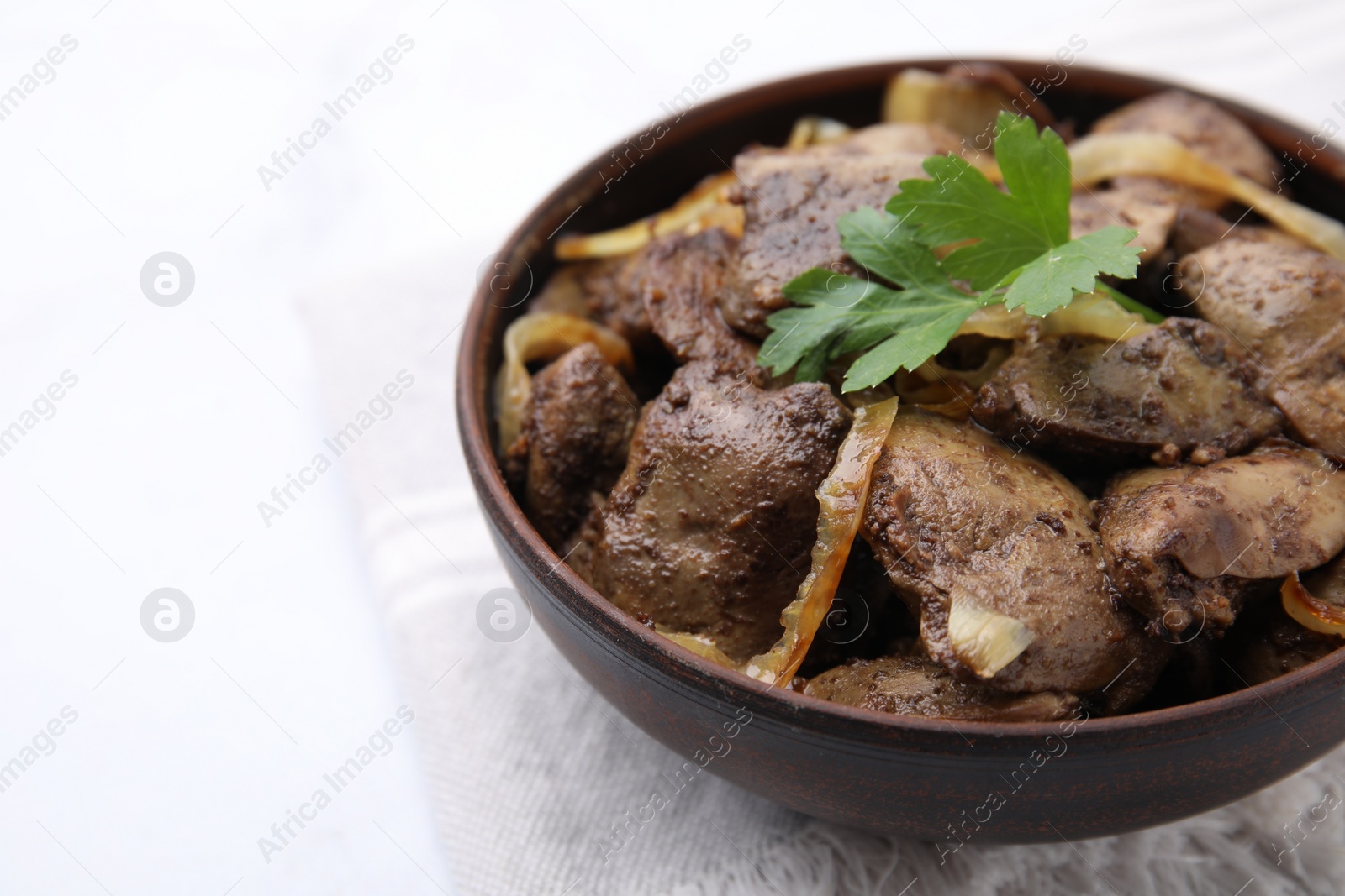 Photo of Tasty fried chicken liver with onion and parsley in bowl on white table, closeup. Space for text