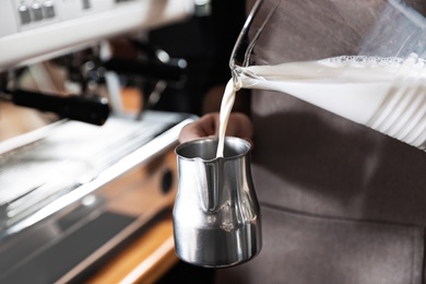 Photo of Barista pouring milk into metal pitcher indoors, closeup with space for text. Coffee making