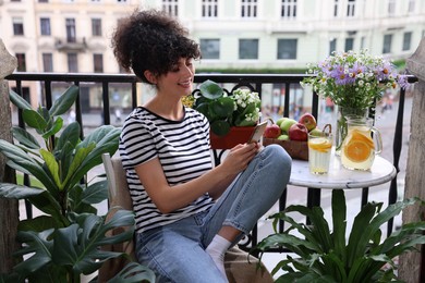 Photo of Beautiful young woman using smartphone at table on balcony with houseplants
