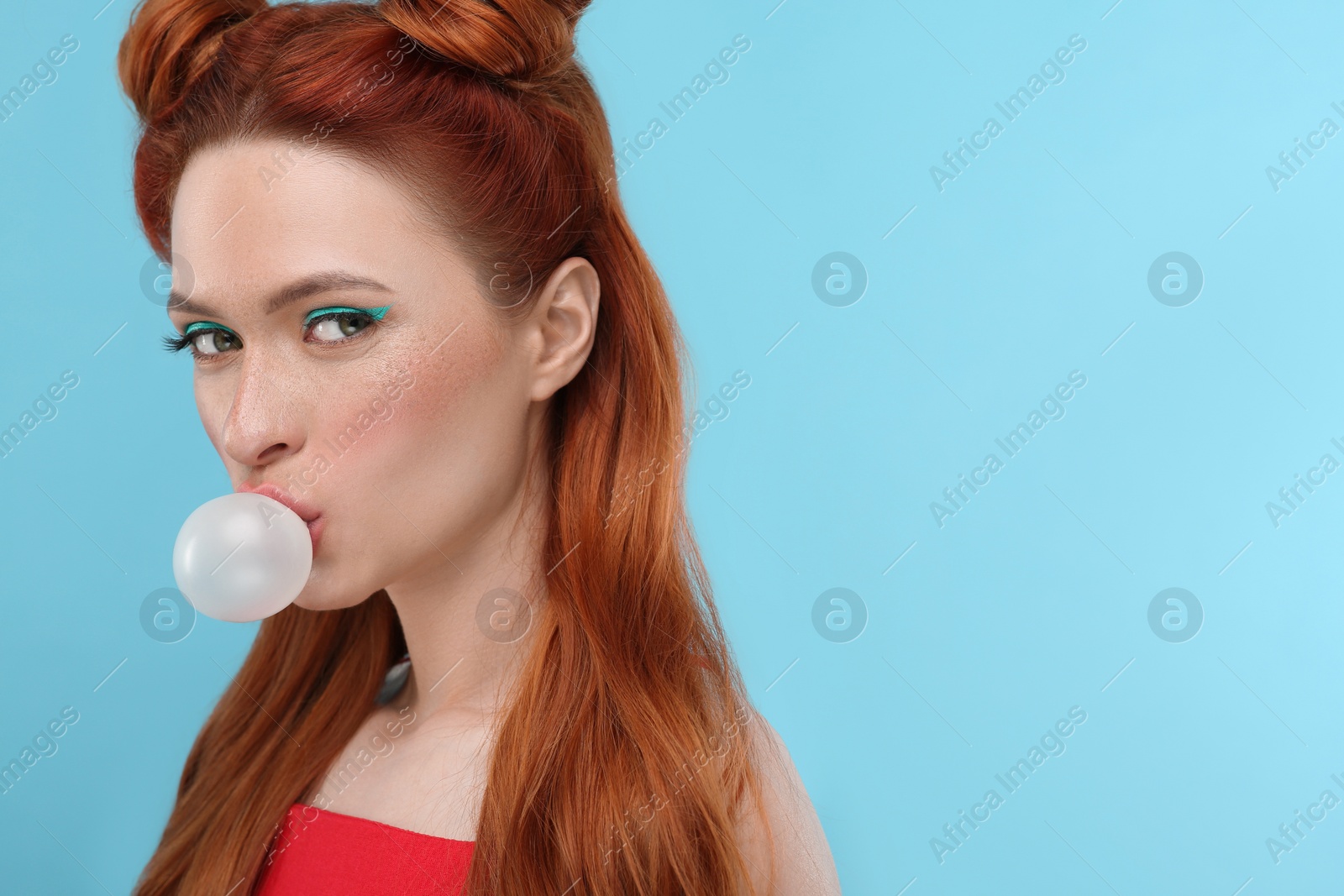 Photo of Beautiful woman with bright makeup blowing bubble gum on light blue background. Space for text