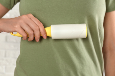 Woman cleaning green t-shirt with lint roller on light background, closeup