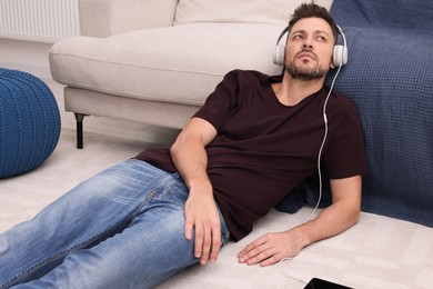 Photo of Upset man listening to music through headphones while lying on floor at home. Loneliness concept