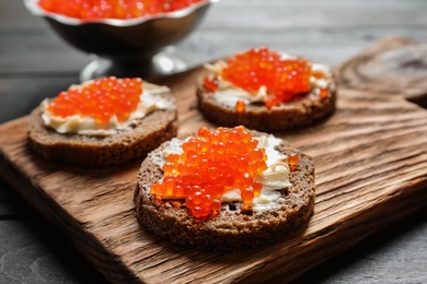 Photo of Delicious sandwiches with red caviar on wooden board