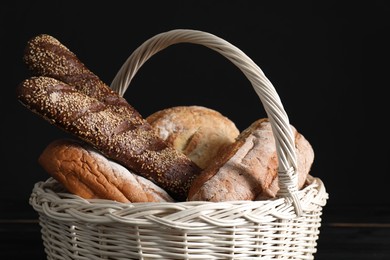 Photo of Wicker basket with different types of fresh bread on black table