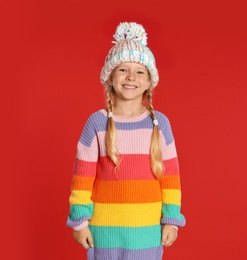 Cute little girl in hat and warm sweater on red background. Winter season