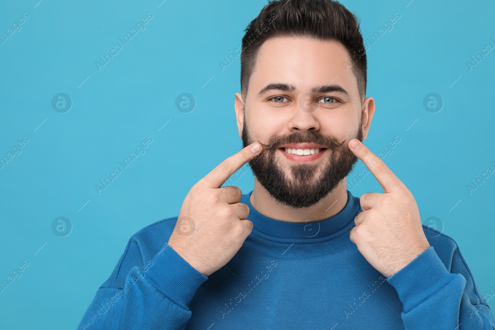 Photo of Happy young man touching mustache on light blue background