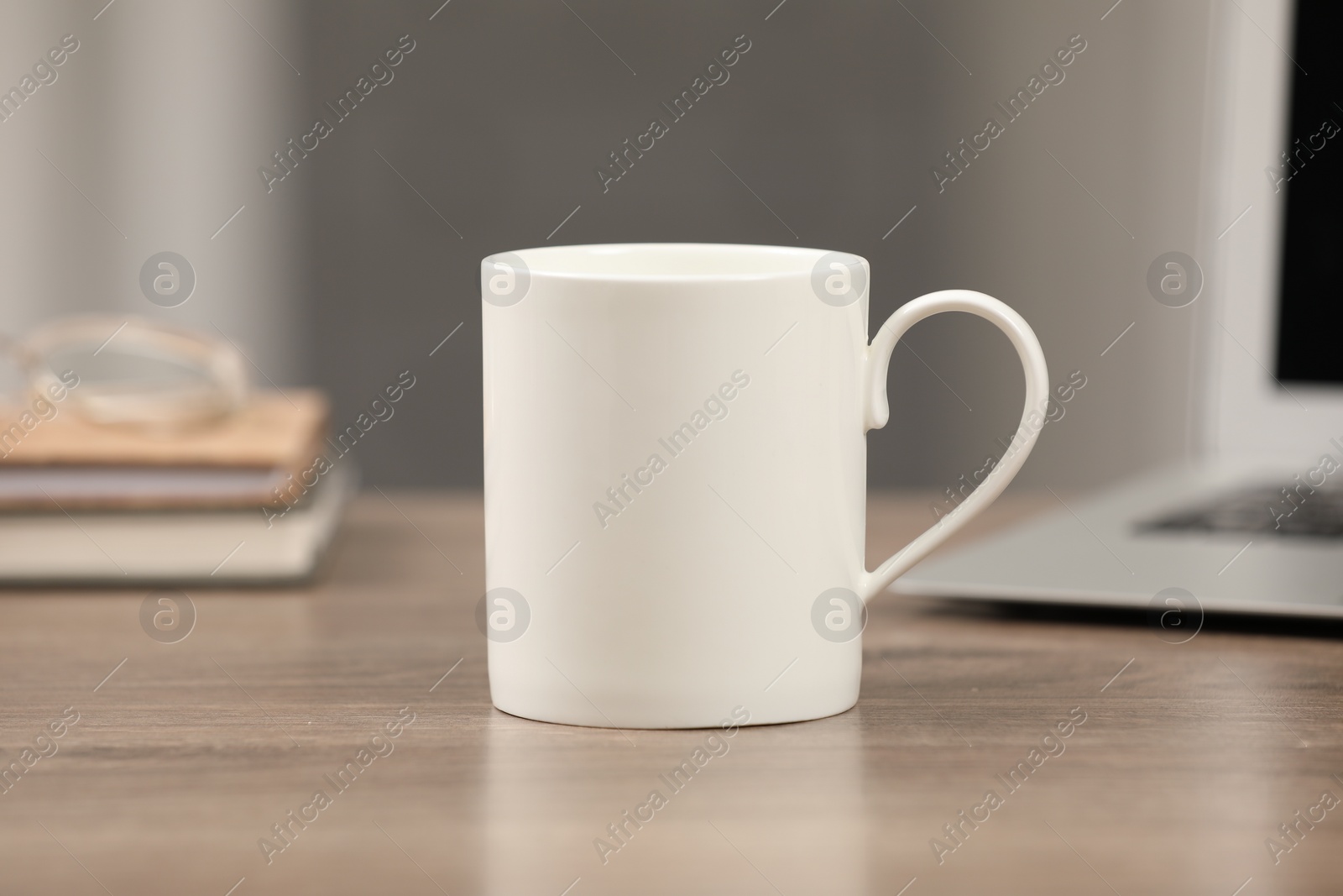 Photo of White ceramic mug on wooden table at workplace