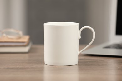 Photo of White ceramic mug on wooden table at workplace