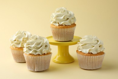 Photo of Tasty vanilla cupcakes with cream on pale yellow background, closeup