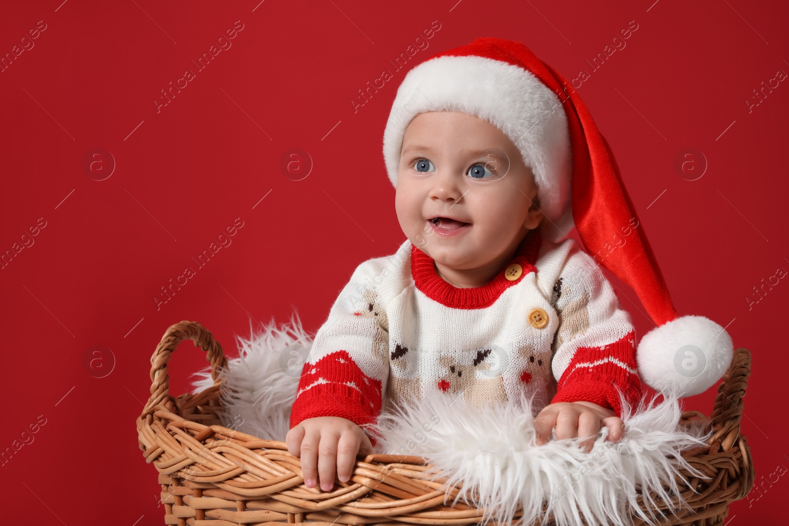 Photo of Cute baby in wicker basket on red background. Christmas celebration