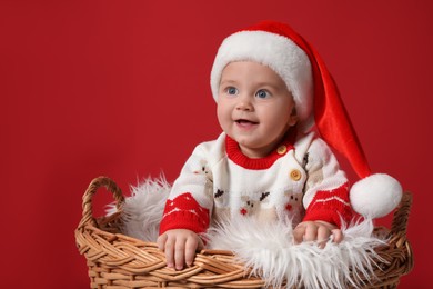 Cute baby in wicker basket on red background. Christmas celebration