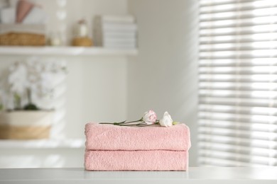 Photo of Stack of clean soft towels with eustoma flowers on white table indoors