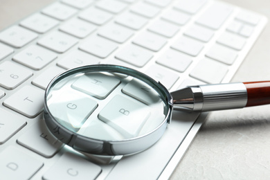 Magnifying glass and computer keyboard on light grey marble table, closeup. Search concept