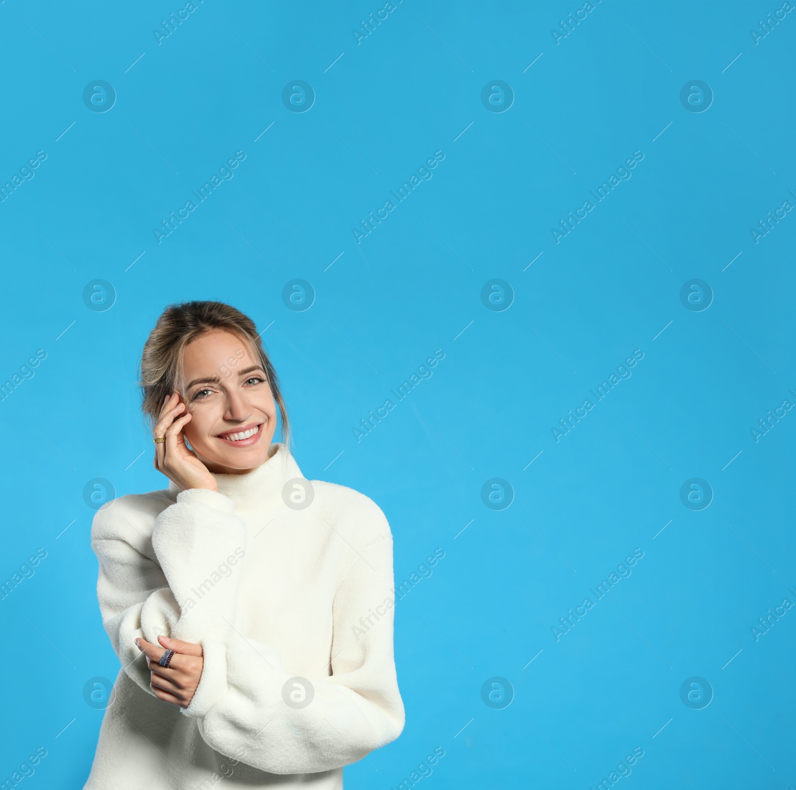 Photo of Beautiful young woman wearing knitted sweater on light blue background. Space for text