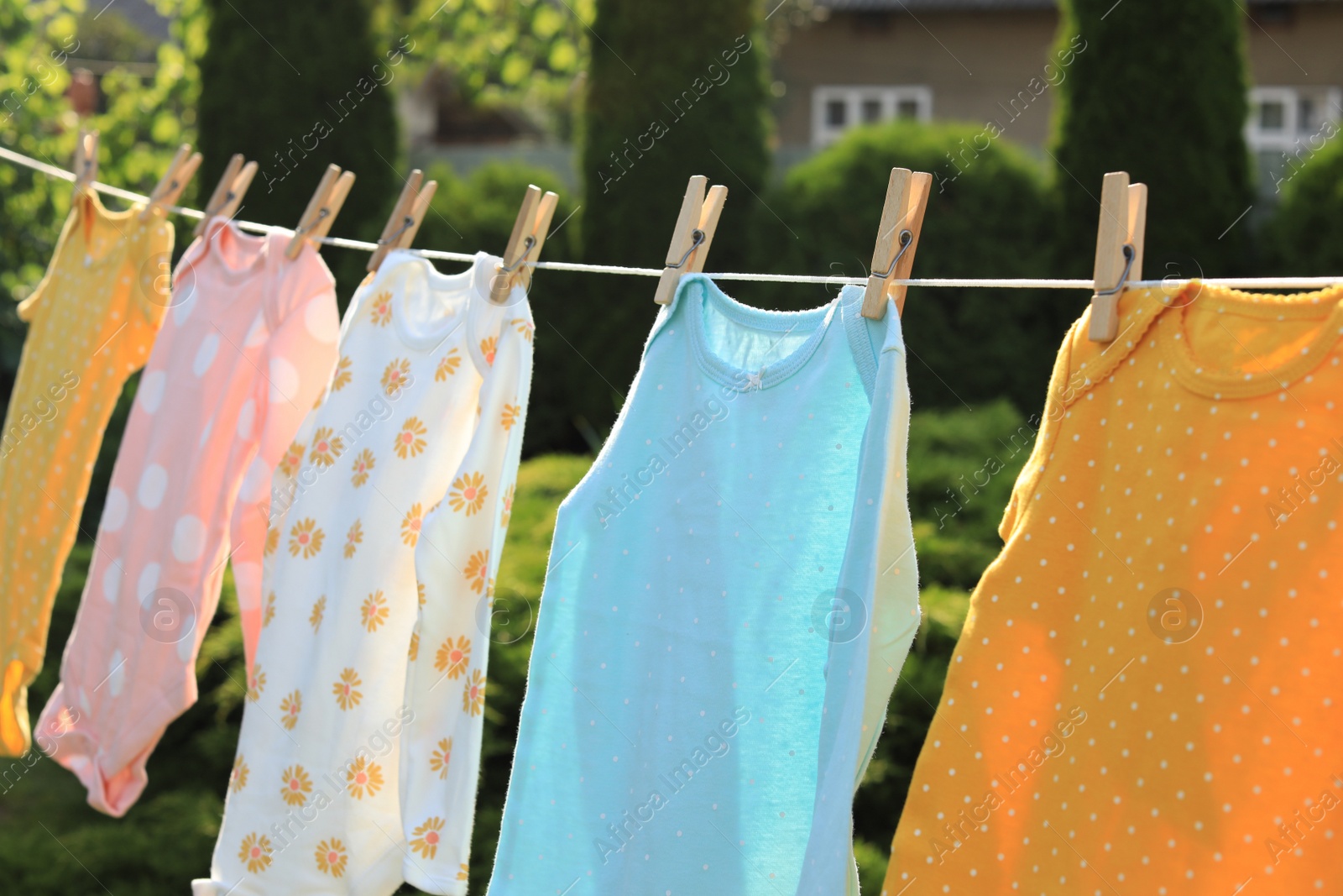 Photo of Clean baby onesies hanging on washing line in garden. Drying clothes