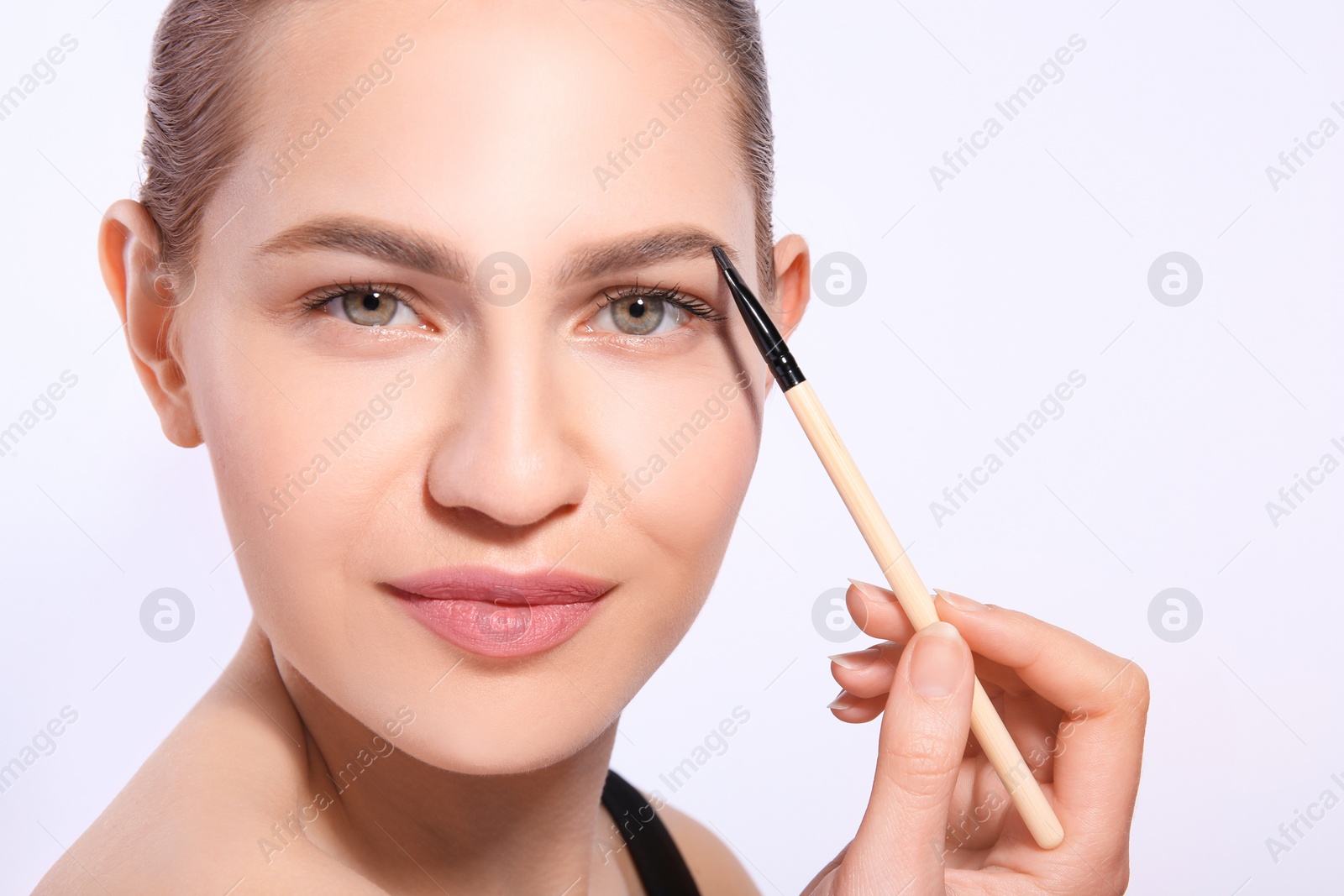 Photo of Beautiful woman with perfect eyebrows applying makeup on light background