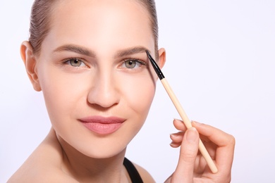 Photo of Beautiful woman with perfect eyebrows applying makeup on light background