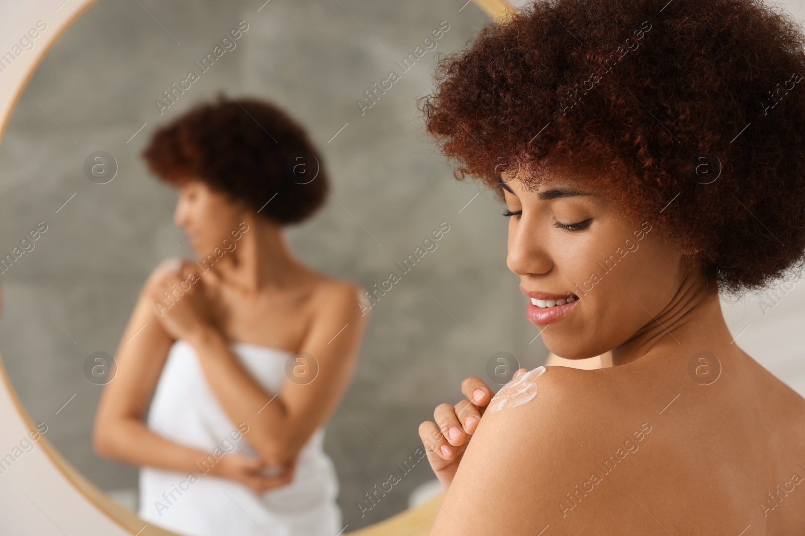 Photo of Beautiful young woman applying body cream onto shoulder indoors