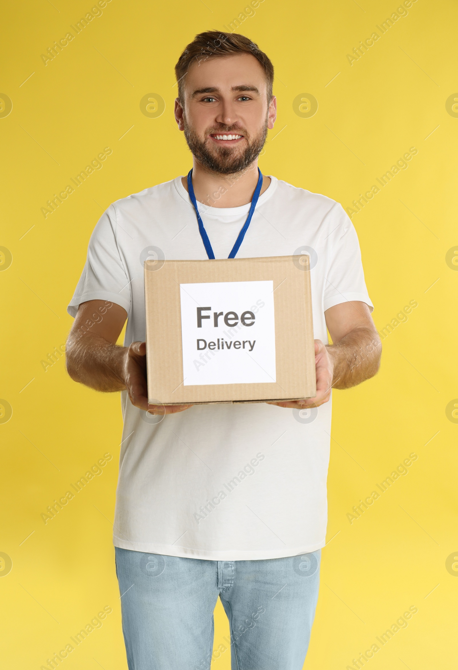 Photo of Male courier holding parcel with sticker Free Delivery on yellow background