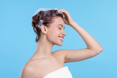 Happy young woman washing her hair with shampoo on light blue background
