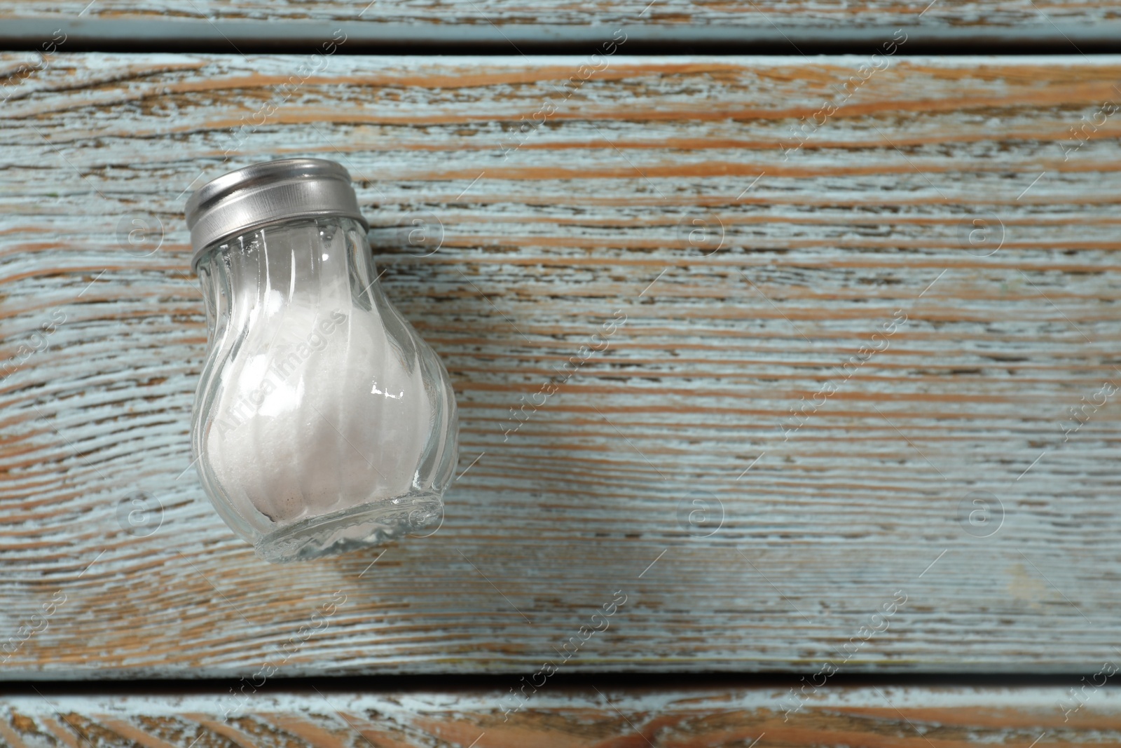 Photo of Salt shaker on light blue wooden table, top view. Space for text