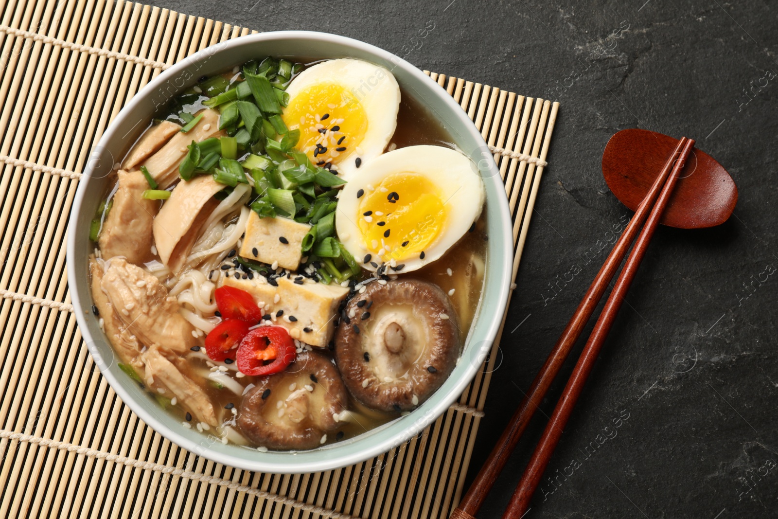 Photo of Noodle soup. Bowl of delicious ramen, ingredients and chopsticks on black table, top view