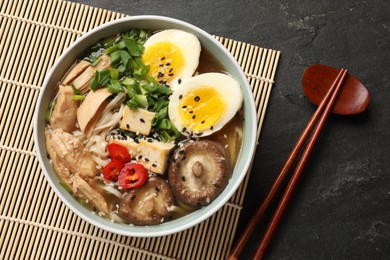 Noodle soup. Bowl of delicious ramen, ingredients and chopsticks on black table, top view