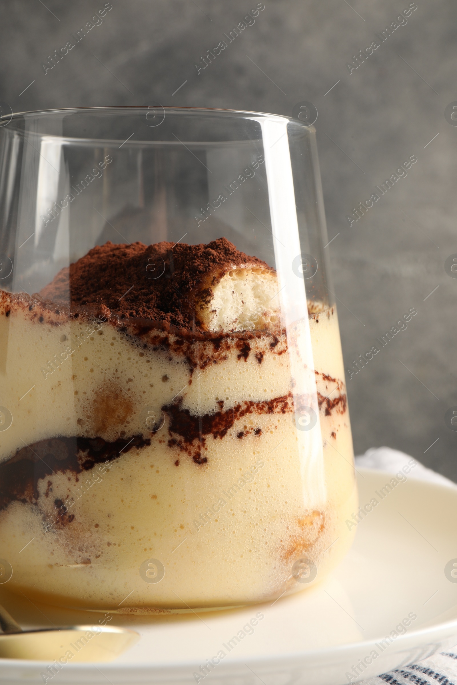 Photo of Delicious tiramisu in glass on plate, closeup