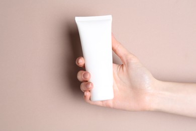 Photo of Woman with tube of cream on beige background, closeup