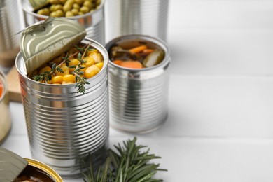 Open tin cans with corn kernels and different products on white table, closeup. Space for text