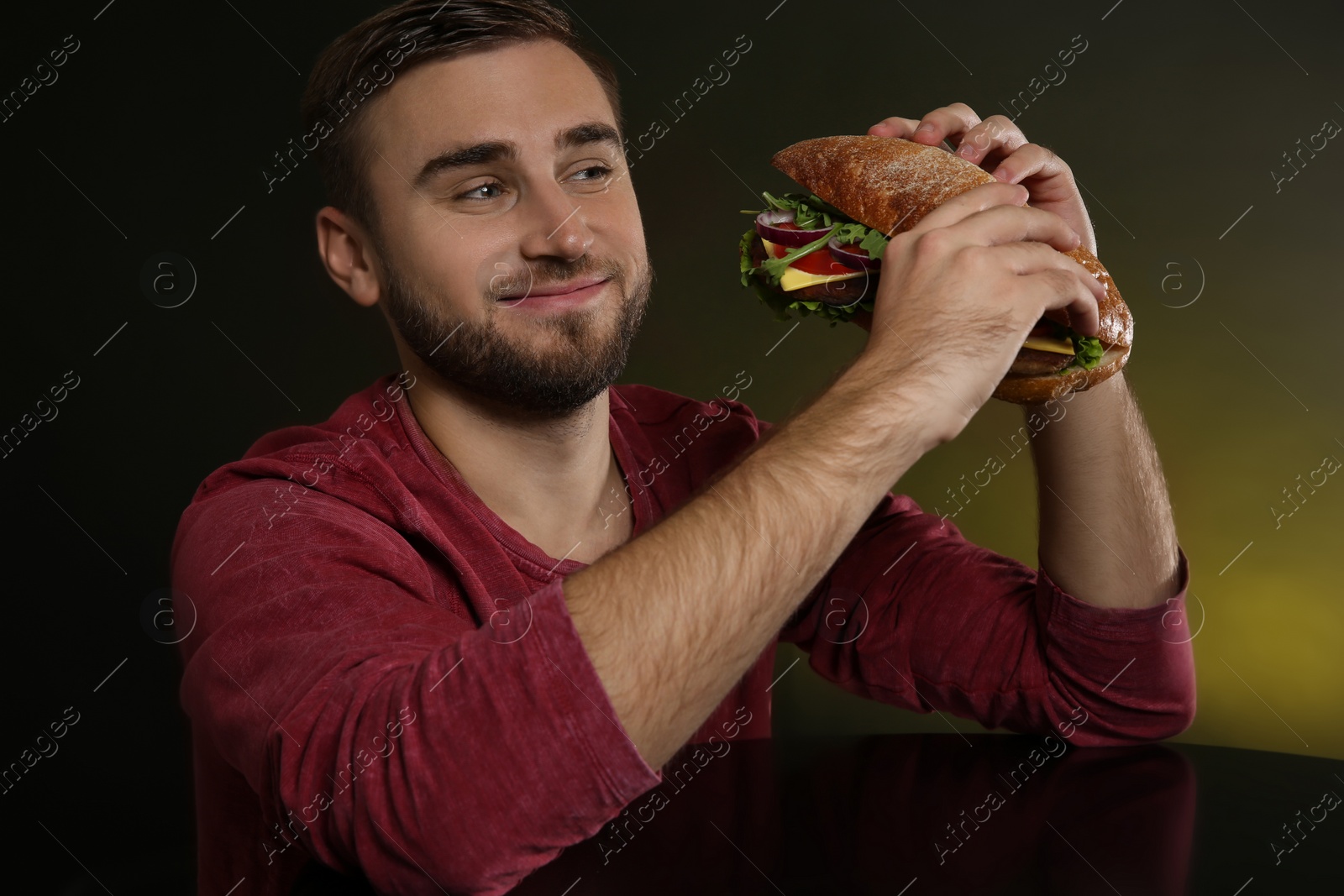 Photo of Young hungry man with tasty burger on color background