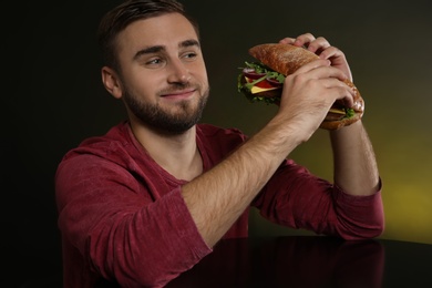 Photo of Young hungry man with tasty burger on color background