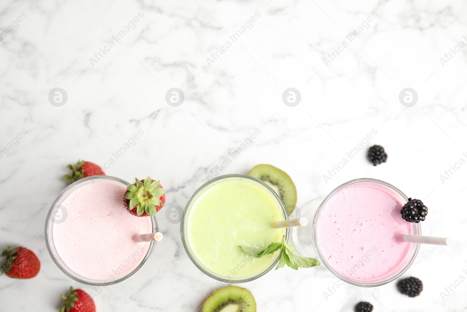 Photo of Tasty fresh milk shakes with fresh berries on white marble table, flat lay. Space for text