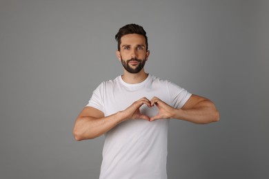 Man making heart with hands on grey background