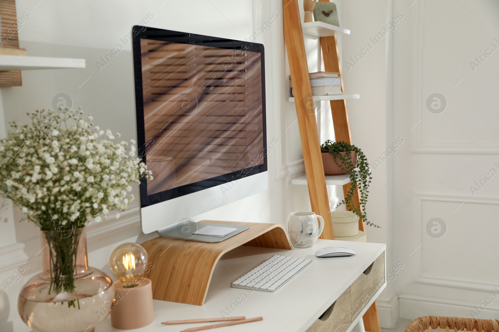 Photo of Comfortable workplace with modern computer and beautiful flowers in room. Interior design