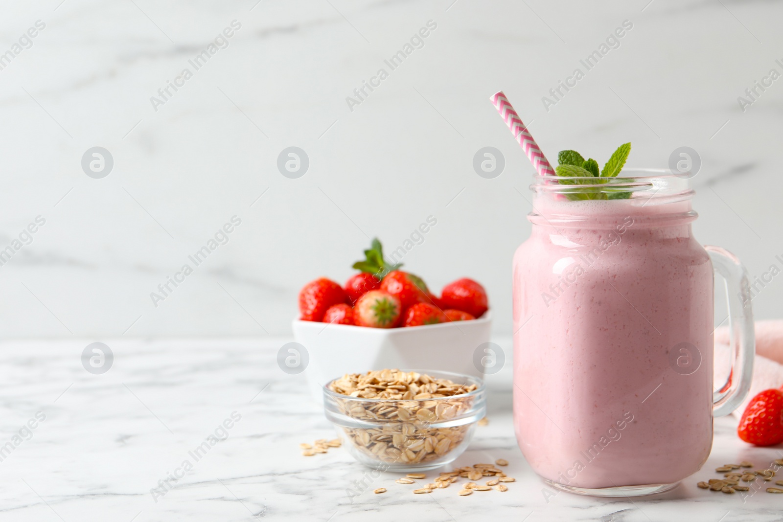 Photo of Mason jar of tasty strawberry smoothie with oatmeal and mint on white marble table, space for text