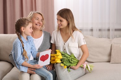 Photo of Little girl congratulating her mom and granny with flowers and postcard at home. Happy Mother's Day
